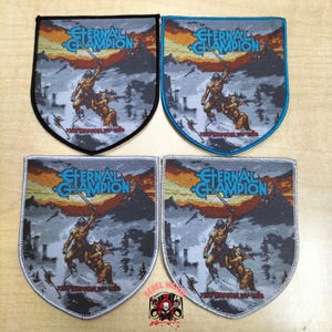 Op de afbeelding: Vier schildvormige stoffen patches met het Eternal Champion logo en de tekst The Armor of Ire. Elke patch toont een krijgersfiguur met een zwaard tegen een berglandschap. De randen zijn zwart, blauw, lichtgrijs en donkergrijs van kleur.