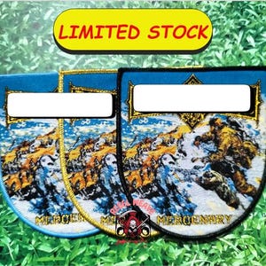 May include: Embroidered patches with a shield shape, featuring a detailed illustration of a figure in a snowy landscape. The patches have a blue background with gold trim and the word "MERCENARY" at the bottom. The text "LIMITED STOCK" is at the top.