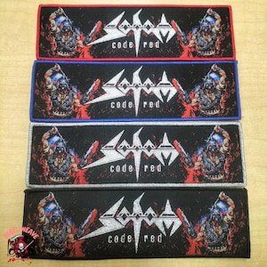 May include: Rectangular embroidered patches with the text "Sodom code red" in white. The patches feature a red, blue, and black border. The design includes a skull and a stylized logo.