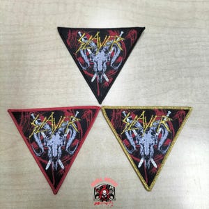 May include: Three triangular embroidered patches featuring the Slayer logo in yellow text above a grey ram skull graphic on a black background with red accents. The patches have black, red, and gold stitched borders respectively.