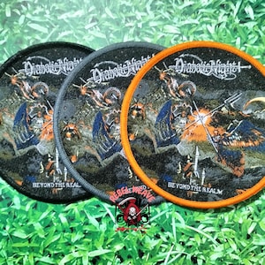 Könnte beinhalten: Drei runde gestickte Aufnäher mit dem Text Diabolic Night und Beyond the Realm. Das Motiv zeigt eine dunkle Landschaft mit einer Figur, die einen Dreizack hält, einen Halbmond und orangefarbene Flammen. Die Ränder sind schwarz, grau und orange.
