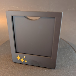 May include: A black picture frame with a gold star design on the bottom. The frame is standing upright on a black surface.