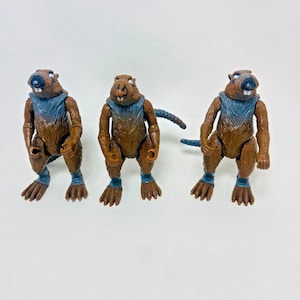 May include: Three brown action figures of beaver-like creatures with blue accents on their necks and ankles. The figures have detailed fur textures and are posed in a standing position, with their arms bent and their tails visible.
