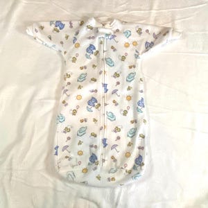 May include: White baby sleep sack with a colorful pattern of elephants, umbrellas, and suns. The sleep sack has short sleeves, a full-length zipper, and a round neckline. The sleep sack is designed to keep babies warm and comfortable.