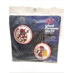May include: A vintage "Crewel Christmas Idea Kit" in a plastic package. The kit includes two 4-inch diameter embroidered Christmas ornaments with mouse designs. The ornaments have red and white accents and gold hanging strings.