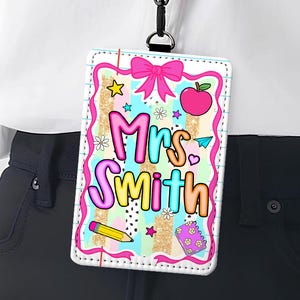 May include: A colorful teacher ID badge with the name "Mrs. Smith" in bubble letters. The badge features a pink bow, apple, pencil, and stars on a striped background. It is hanging from a black lanyard.