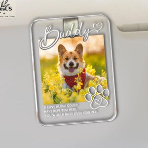 May include: A rectangular clear acrylic car visor clip featuring a photograph of a Corgi dog wearing a red bandana in a field of yellow flowers. The text Buddy is printed at the top, and the phrase If love alone could have kept you here, you would have lived forever is printed at the bottom with a white paw print icon.