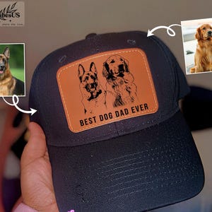 May include: Black baseball cap with a brown leather patch featuring a German Shepherd and Golden Retriever illustration, with the text "BEST DOG DAD EVER". The cap has a curved brim and a structured crown.