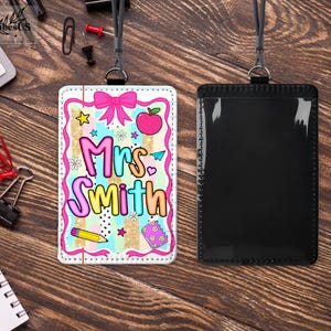 May include: A teacher's ID badge with a colorful design. The badge features the name "Mrs. Smith" in a playful font, along with illustrations of an apple, bow, star, and pencil. The badge is paired with a black lanyard and a clear ID holder.
