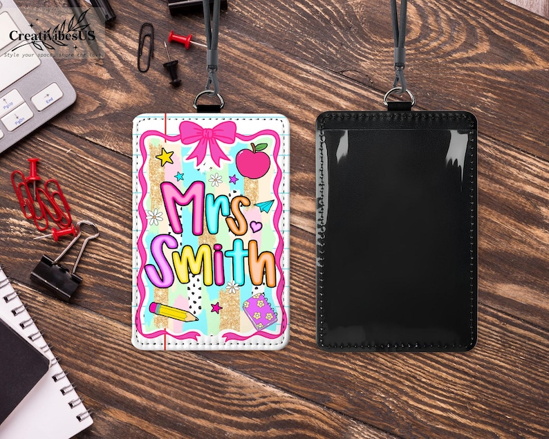 May include: A teacher's ID badge with a colorful design. The badge features the name "Mrs. Smith" in a playful font, along with illustrations of an apple, bow, star, and pencil. The badge is paired with a black lanyard and a clear ID holder.
