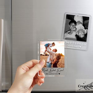 K&ouml;nnte beinhalten: Zwei rechteckige Fotomagnete aus klarem Acryl. Ein Magnet zeigt ein Farbfoto einer Person, die ein Kind hochhebt, mit dem Text "Best Dad Ever! WE LOVE YOU" am unteren Rand. Der andere Magnet zeigt ein Schwarz-Wei&szlig;-Foto mit Text.