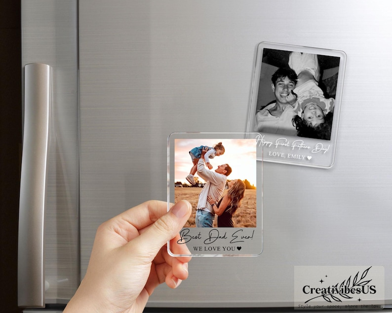 K&ouml;nnte beinhalten: Zwei rechteckige Fotomagnete aus klarem Acryl. Ein Magnet zeigt ein Farbfoto einer Person, die ein Kind hochhebt, mit dem Text "Best Dad Ever! WE LOVE YOU" am unteren Rand. Der andere Magnet zeigt ein Schwarz-Wei&szlig;-Foto mit Text.