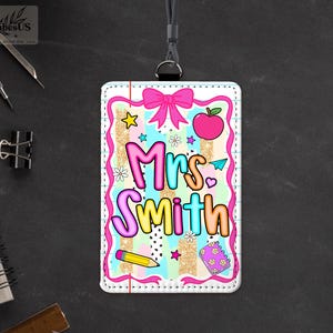 May include: A colorful teacher ID badge with the name "Mrs. Smith" in bubble letters. The badge features a pink bow, apple, stars, and pencil graphics. The badge is on a black lanyard.