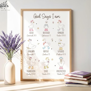 May include: A framed print with the text "God Says I Am" and illustrations of ducks with various affirmations like "Love" and "Blessed." The artwork features a light wood frame and is accompanied by a vase of lavender and a stack of books.