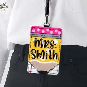 K&ouml;nnte beinhalten: Ein gelber, stiftf&ouml;rmiger Ausweishalter mit dem Namen "Mrs. Smith" in schwarzer Schrift. Die Oberseite hat rosa Tupfen und ein schwarzes Schl&uuml;sselband. Das Abzeichen h&auml;ngt an einem schwarzen Schl&uuml;sselband.