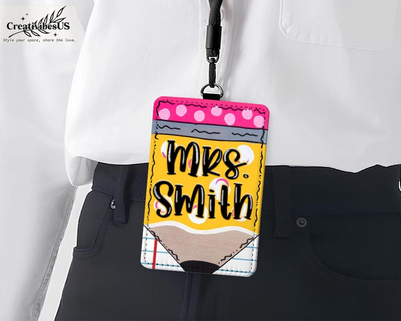 K&ouml;nnte beinhalten: Ein gelber, stiftf&ouml;rmiger Ausweishalter mit dem Namen "Mrs. Smith" in schwarzer Schrift. Die Oberseite hat rosa Tupfen und ein schwarzes Schl&uuml;sselband. Das Abzeichen h&auml;ngt an einem schwarzen Schl&uuml;sselband.