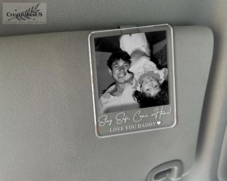 K&ouml;nnte beinhalten: Ein rechteckiger, durchsichtiger Acryl-Clip f&uuml;r die Sonnenblende im Auto mit einem Schwarz-Wei&szlig;-Foto eines Erwachsenen und eines Kindes. Der Text "Stay Safe, Come Home!" und "LOVE YOU DADDY" mit einem kleinen Herzsymbol ist unten wei&szlig; aufgedruckt.