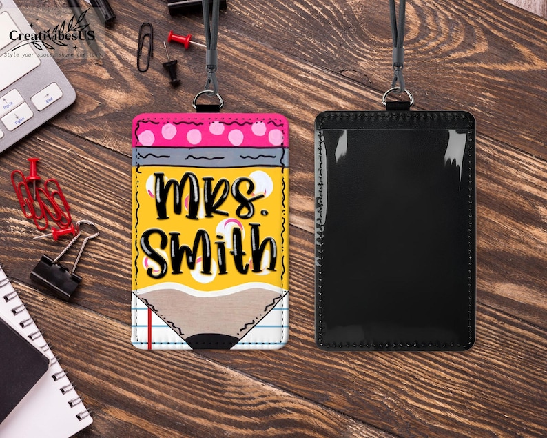 K&ouml;nnte beinhalten: Ein personalisierter Lehrer-Ausweishalter mit Bleistift-Design. Der Ausweishalter tr&auml;gt den Namen "MRS. SMITH" in fetten, schwarzen Buchstaben auf gelbem Hintergrund. Das Design umfasst rosa Punkte, Grau und eine Bleistiftspitze. Ein schwarzes Schl&uuml;sselband ist befestigt.