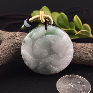 May include: Round jade pendant with a carved fox design. The pendant is primarily white with green accents and is suspended from a brown cord with a gold-colored loop. A US quarter is in the foreground.