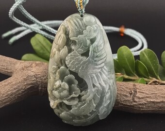 May include: A jade pendant with a carved phoenix and floral design. The pendant is a mix of green and white hues, suspended from a light green cord. The intricate carving showcases the bird and flowers.