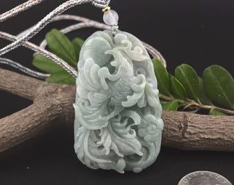 May include: A carved jade pendant with a floral and bird design. The pendant is a light green color and is suspended from a woven cord. The pendant is approximately 2 inches long.