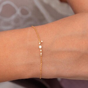 Könnte beinhalten: Ein zartes Armband aus goldener Kette mit einem Konstellationsdesign, das mit kleinen funkelnden Steinen besetzt ist.