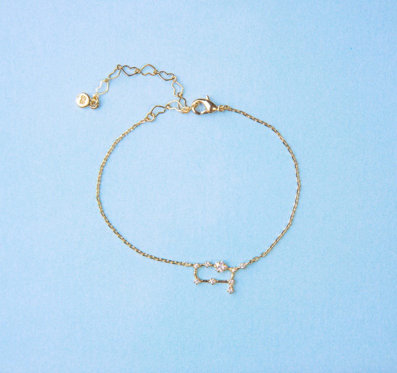 Puede incluir: Un brazalete de cadena dorada con un dije de constelaci&oacute;n G&eacute;minis hecho de peque&ntilde;os cristales transparentes.
