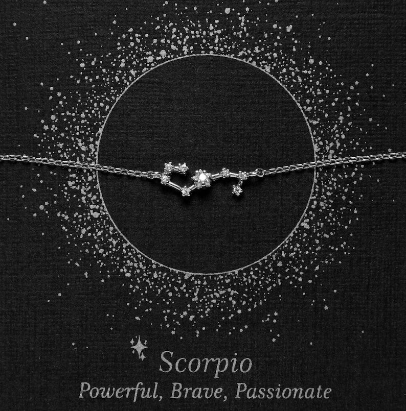 May include: A silver necklace with a constellation design representing the zodiac sign Scorpio. The necklace is on a black background with a circle of white dots around it. The text "Scorpio" and "Powerful, Brave, Passionate" is below the necklace.