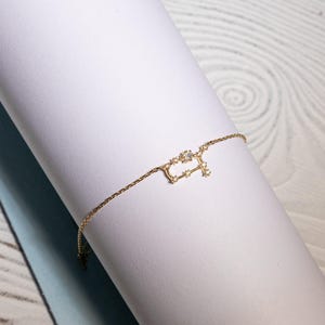 Puede incluir: Un brazalete de cadena dorada con un delicado dise&ntilde;o de constelaci&oacute;n con peque&ntilde;as piedras brillantes.