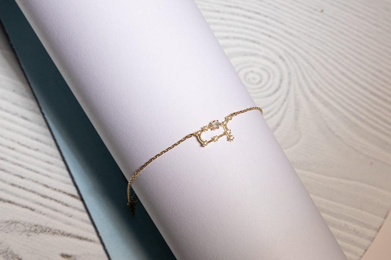 Puede incluir: Un brazalete de cadena dorada con un delicado dise&ntilde;o de constelaci&oacute;n con peque&ntilde;as piedras brillantes.