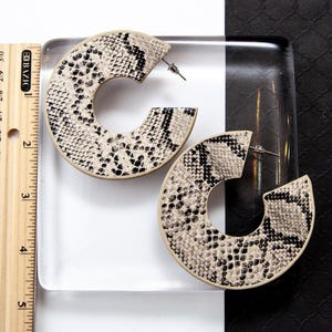 Puede incluir: Un par de pendientes grandes de aro con un patr&oacute;n de piel de serpiente beige y negro.