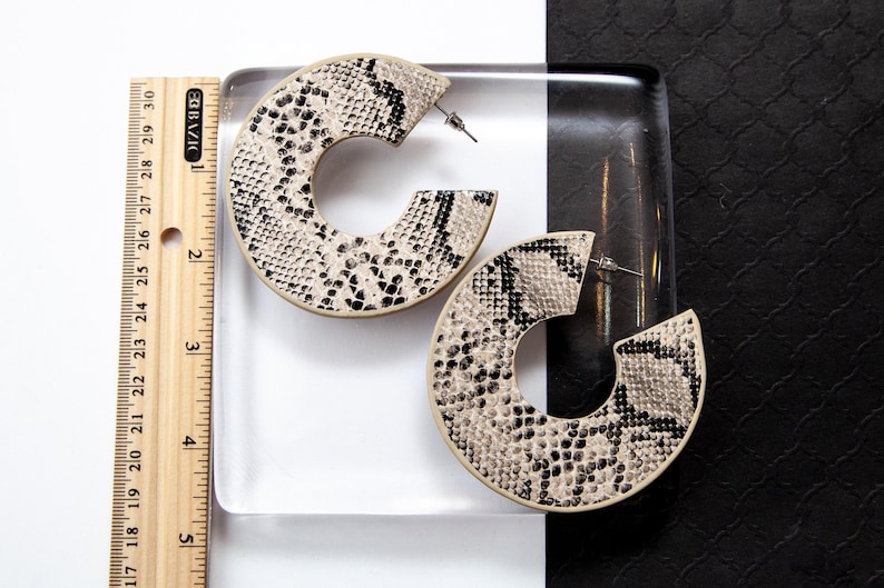Puede incluir: Un par de pendientes grandes de aro con un patr&oacute;n de piel de serpiente beige y negro.