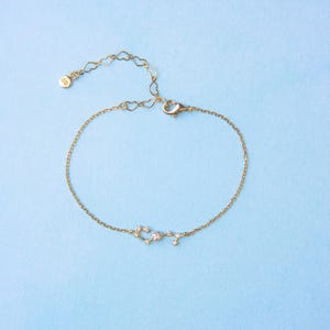May include: A gold chain bracelet with a constellation design featuring small clear stones. The bracelet has a lobster clasp closure.