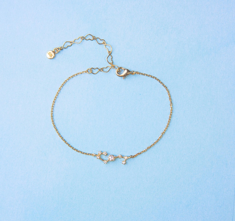 May include: A gold chain bracelet with a constellation design featuring small clear stones. The bracelet has a lobster clasp closure.