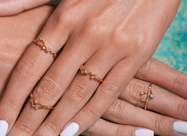 May include: A hand model wearing three gold rings with small diamonds set in the shape of constellations.