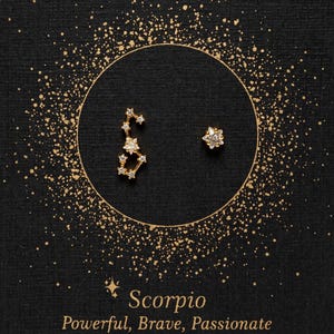 Pode incluir: Brincos de constelação dourados com o signo do zodíaco Escorpião e um brinco de estrela individual. Os brincos estão sobre um fundo preto com glitter dourado. O texto "Scorpio Powerful, Brave, Passionate" está abaixo dos brincos.