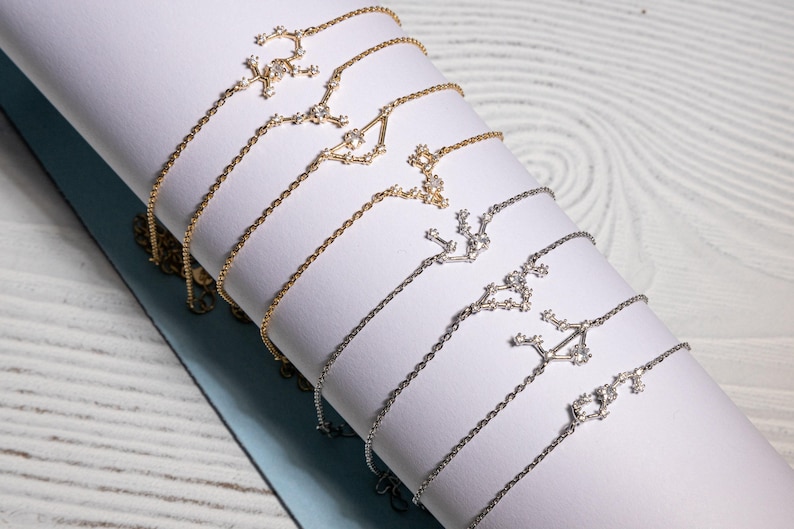 Puede incluir: Un conjunto de delicados collares de plata y oro con dise&ntilde;os de constelaciones. Cada collar tiene una constelaci&oacute;n diferente, con peque&ntilde;as piedras brillantes que representan las estrellas.