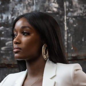 Puede incluir: Una mujer con cabello casta&ntilde;o oscuro que lleva una chaqueta blanca y un par de pendientes grandes, redondos, con estampado de piel de serpiente.