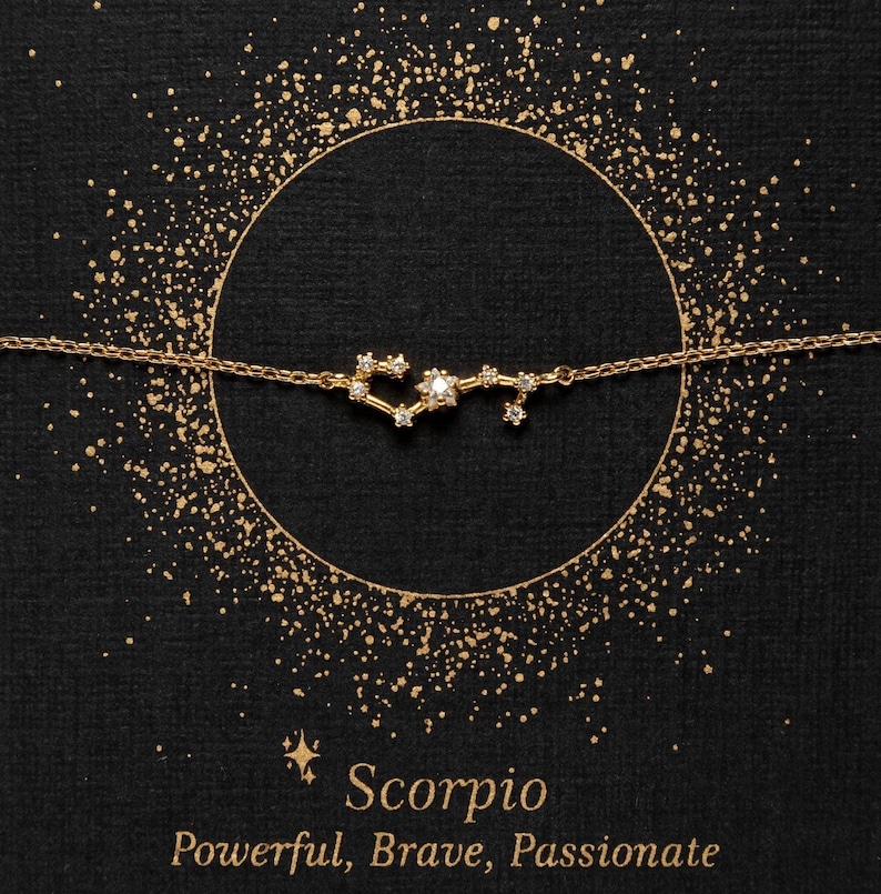 May include: Gold necklace with a constellation of diamonds representing the Scorpio zodiac sign. The necklace is on a black background with gold glitter. The text "Scorpio" and "Powerful, Brave, Passionate" is below the necklace.