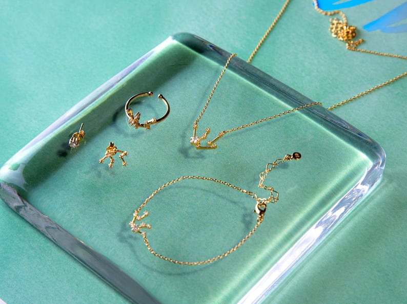 May include: A set of gold jewelry featuring a necklace, bracelet, ring, and earrings. Each piece is adorned with a delicate constellation design with small sparkling stones.