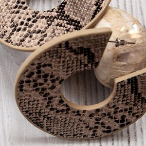 Puede incluir: Un par de pendientes grandes de aro con un patr&oacute;n de piel de serpiente marr&oacute;n y negro.