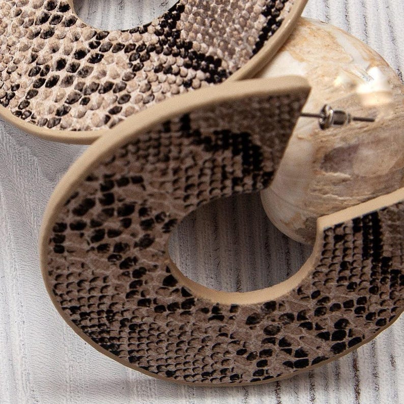 Puede incluir: Un par de pendientes grandes de aro con un patr&oacute;n de piel de serpiente marr&oacute;n y negro.