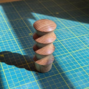 May include: A wooden knob with a spiral design. The knob is made of light brown wood and has a smooth finish.