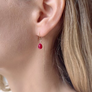 May include: A pair of gold dangle earrings with a single red gemstone on each earring.