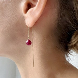 May include: Gold chain earrings with a dangling red gemstone. The earrings are simple and elegant.