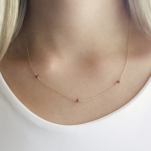 May include: A delicate gold chain necklace with three small red gemstone accents.