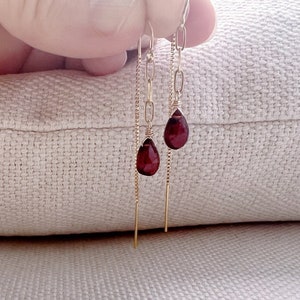 May include: A pair of gold dangle earrings with red gemstone drops. The earrings feature a delicate chain and a simple, elegant design.
