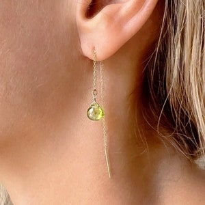 May include: Gold chain earrings with a green gemstone pendant. The earrings are long and dangle from the earlobe.
