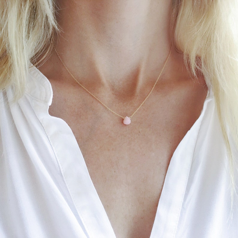 Pu&ograve; includere: Una delicata collana a catena dorata con un piccolo ciondolo a forma di lacrima in opale rosa.