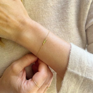 Op de afbeelding: Een delicate gouden kettingarmband met een kleine cluster groene edelstenen.